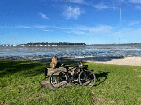 Image of Cindy sitting on a bench looking at a lake, bicycle behind her.