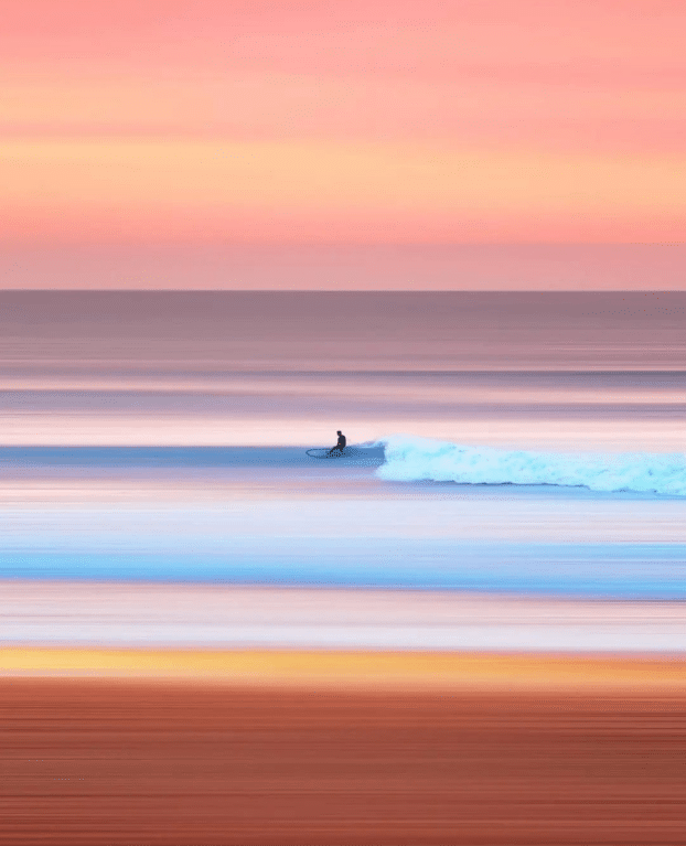 Man surfing, calm beach, one wave. Sunset colors.