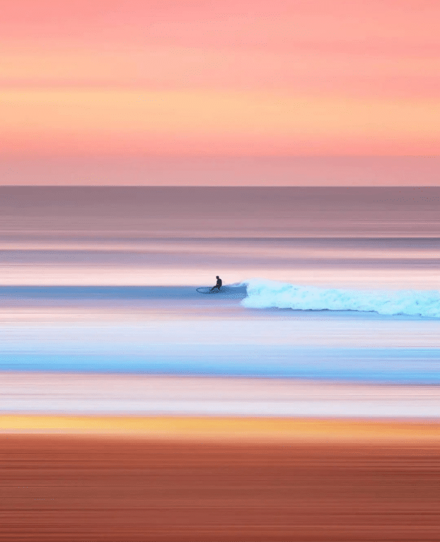 Man surfing, calm beach, one wave. Sunset colors. 