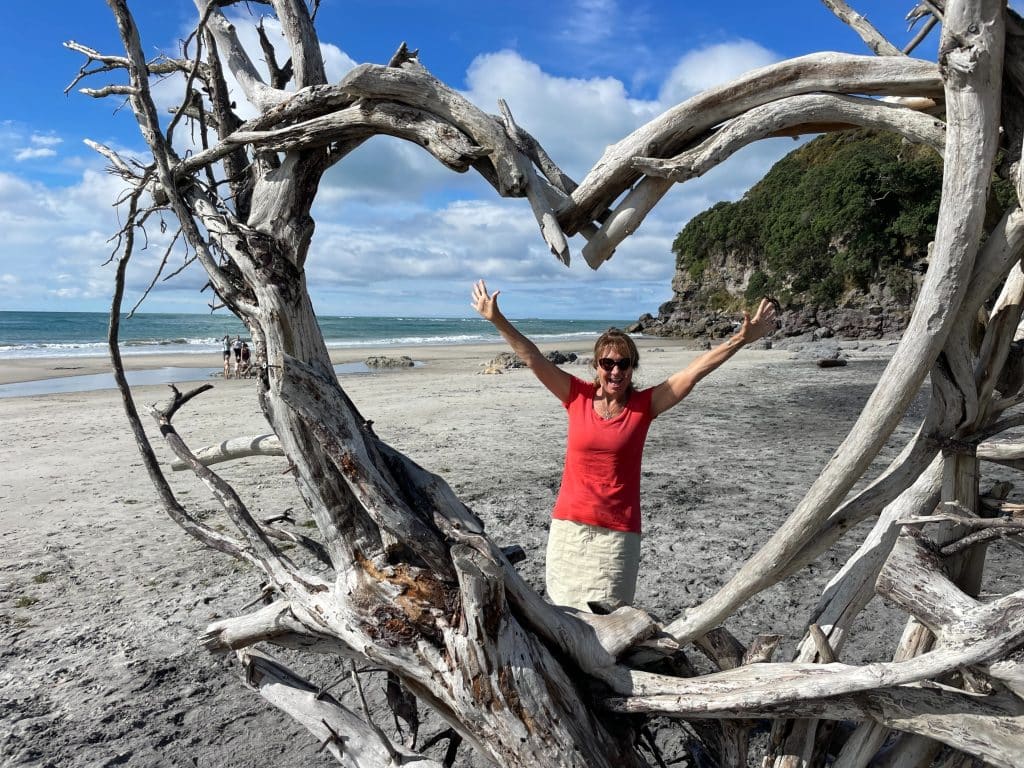 Cindy on the beach standing in a heart made of driftwood.